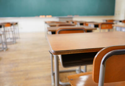 Empty desks in a classroom with a blackboard in the background.