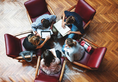 Group of people gathered around in a circle looking at various materials in front of them.